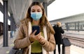 People with surgical mask using smartphone at train station Royalty Free Stock Photo