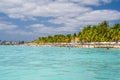 People swimming near white sand beach with umbrellas, bungalow bar and cocos palms, turquoise caribbean sea, Isla Mujeres island,