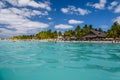 People swimming near white sand beach with umbrellas, bungalow bar and cocos palms, turquoise caribbean sea, Isla Mujeres island,