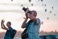 2 people taking with there smartphone and DSLR camera pictures of the climbing hot air balloons while the sky turns red.