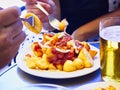 People taste a portion of Patatas Bravas over a metallic table. Fried potatoes topped with spicy sauce, also know as Patatas a la