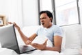 Angry indian man with laptop in bed at home
