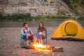 People, tourism and nature concept - Romantic evening, man embrace woman sitting near a campfire