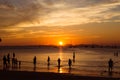 People, tourists enjoy a gorgeous sunset on a tropical beach. Silhouettes of people are all watching the sun. Golden tones. The Royalty Free Stock Photo
