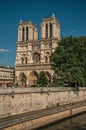 People, tree-lined Seine River and gothic Notre-Dame Cathedral at Paris.
