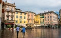People with umbrellas on rainy overcast day on Piazza della Riforma square with colorful buildings in Lugano Ticino Switzerland