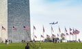 People visiting the Washington Monument with a commercial airplane landing in the background