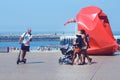 People walk along the promenade of Ostend. Large red metal structures resembling crumpled bags. Belgium.
