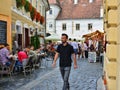 People walk on a narrow street with outdoor restaurant cafe