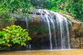 People walk under a waterfall in a tropical forest with green trees in summer