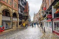 People walking along a cobbled street lined with historic architecture and shops in Chester, England, on a cloudy summer day Royalty Free Stock Photo