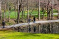 People walking along a smooth footpath in the garden near a lake surrounded by lush green grass and bare winter trees Royalty Free Stock Photo