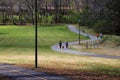 People walking along winding footpaths in the park surrounded by lush green grass, tall black lamp posts, lush green trees