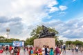 People walking around the Triumph of Labour statue with blue sky and clouds in the background