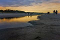 People walking on beach around puddle near water over Baltic Sea in Swinoujscie at sunset