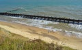 People walking on beach between failing sea defenses and crumbling cliffs.