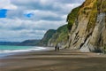 People walking on a deserted beach with towering limestone cliffs.