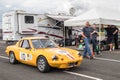 People walking down a paddock looking at a racing car driving past. Motion blur