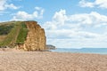 People walking on golden beach underneath towering cliffs on sunny summer day.