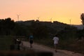 People walking in grassy countryside with windmills in sunset