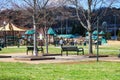 People walking and playing in the park surrounded by lush green grass, bare winter trees, benches, a play ground Royalty Free Stock Photo