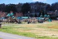 People walking and playing in the park surrounded by lush green grass, bare winter trees, benches, a play ground Royalty Free Stock Photo