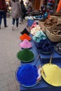 People walking by red, yellow, orange, blue, and other variety of colorful spices fore sale in Jemaa el-Fnaa marketplace in