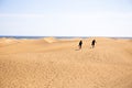 People walking on sand hills near Atlantic ocean against clear blue sky in Maspalomas, Gran Canaria