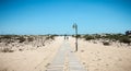 People walking on a small concrete beach path surrounded by fine sand on ilha de tavira, portugal Royalty Free Stock Photo