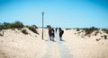 People walking on a small concrete beach path surrounded by fine sand on ilha de tavira, portugal Royalty Free Stock Photo