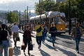 People walking on the street in front of a yellow streetcar