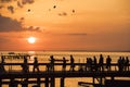 People Walking on Sunset over Bridge. Backlight Shot. Silhouettes of Men, Women, Children and Dog in Front of Lake.