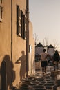 People walking towards windmills during sunset on a street in Hora Mykonos Town, Mykonos, Greece Royalty Free Stock Photo