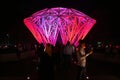 People walking under a big diamond art installation with pink lighting