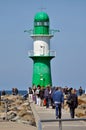 People walking on a wooden pathway towards a green colored lighthouse