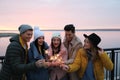 People in warm clothes holding burning sparklers near river