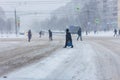 People in winter garment crossing winter street during heavy snowfall in daylight