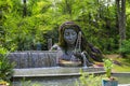 People working on the Earth Goddess with steel ladders surrounded by lush green trees, grass and plants