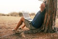 People working outdoor with computer and wireless connection. One man stretching his back against a tree with laptop on the legs. Royalty Free Stock Photo