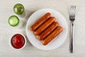 Pepper and salt, bowl with ketchup, fried sausages in white plate, fork on table. Top view