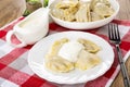 Pepper, sauce boat with sour cream, boiled dumplings in plate, few dumplings with sour cream in plate, fork on napkin on wooden