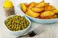 Pepper, bowl with green peas, blue plate with fried potato, fork on wooden table Royalty Free Stock Photo