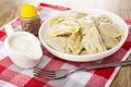 Pepper, sauce boat with sour cream, boiled dumplings in white plate, fork on napkin on wooden table