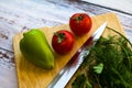 Pepper, two tomatoes, knife and green herbs on wooden board