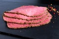 Peppered roast beef slices on stone board with grains of coloured pepper Royalty Free Stock Photo