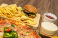 Tasty fast food on table. Pepperoni pizza and pizza Capricciosa , hamburger and potato chips Royalty Free Stock Photo