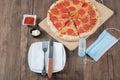 Pepperoni pizza on a wooden board with sauces, hand sanitizer and mask around