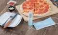 Pepperoni pizza on a wooden board with sauces, plate, hand sanitizer