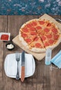 Pepperoni pizza on a wooden board with sauces, plate, hand sanitizer