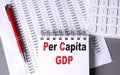 PER CAPITA GDP text on notebook with pen, calculator and chart on grey background Royalty Free Stock Photo